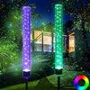Two vertical LED path lights emit vibrant purple and green light in a garden setting.