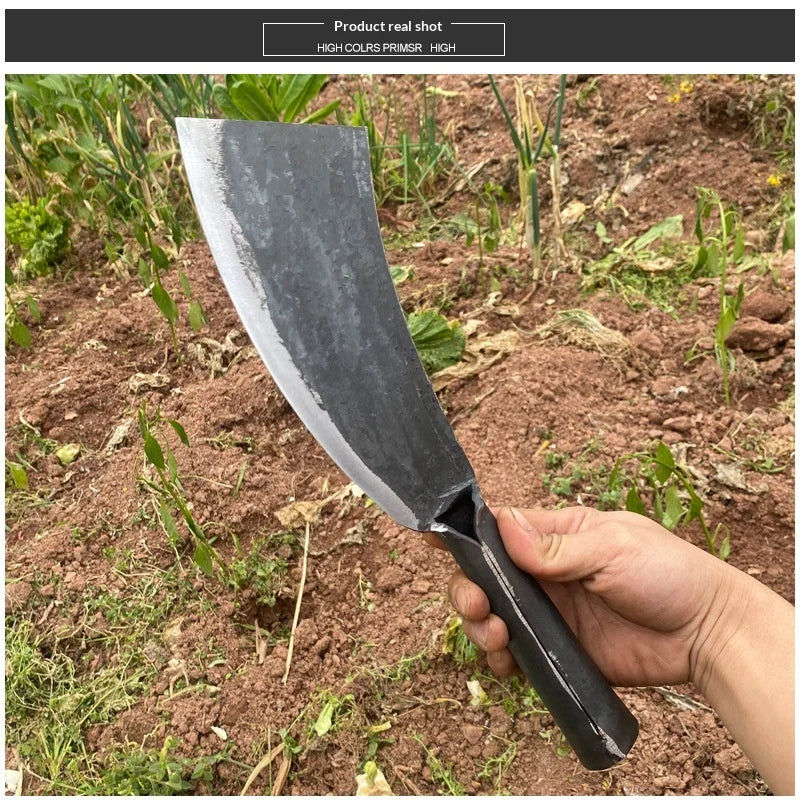 A hand holds a black forged steel axe with a curved blade in a dirt and plant environment.