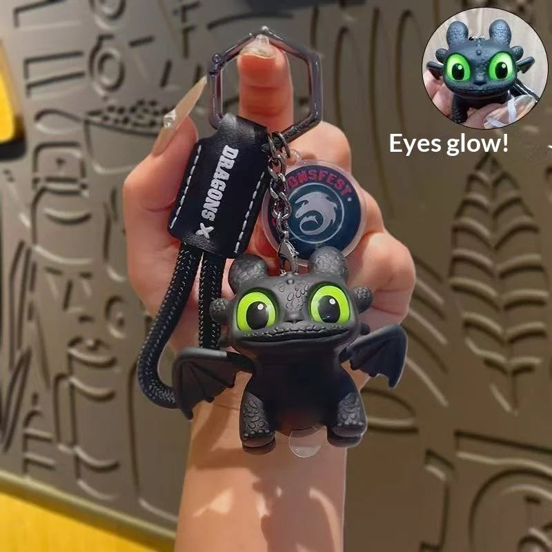 A hand holds a black Toothless Car Ornament with glowing green eyes and movable wings, next to a circular emblem.