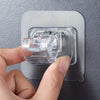 A hand is installing an adhesive curtain rod hook clamp onto a gray wall surface.
