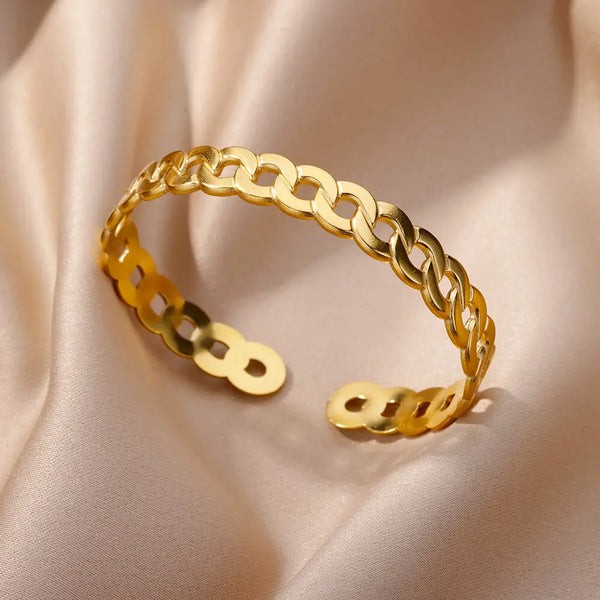 Bracelet de montre ajustable en acier inoxydable doré posé sur un tissu rose pâle.