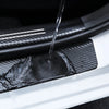 Close-up of a carbon fiber door sill protector sticker being wet with water on a white car body.