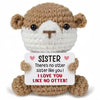 A handmade crochet animal doll with brown fur and white face, holding a card that reads Sister I love you like no otter.