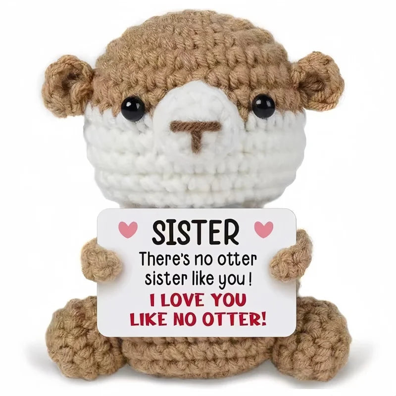 A handmade crochet animal doll with brown fur and white face, holding a card that reads Sister I love you like no otter.