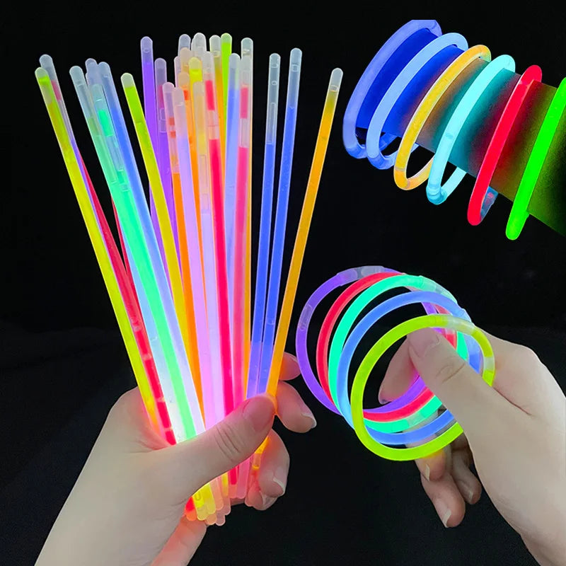 A hand holds a bundle of colorful glow sticks and several bendable glow bracelets.