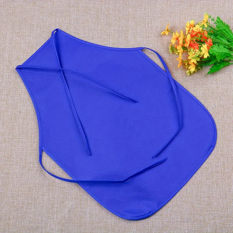 A royal blue non-woven fabric craft apron is displayed on a beige cloth with some yellow flowers.