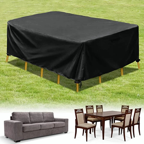 Black waterproof patio furniture cover spread over a table on green grass, next to a wooden dining set.