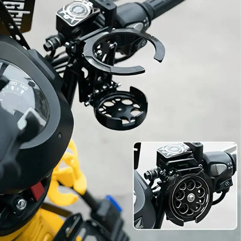 Vista cercana de un soporte plegable negro para vaso de motocicleta montado en el manillar.