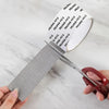 A hand holds a roll of self-adhesive window screen repair tape with various numbered patches on a white marble surface.