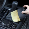 A hand is holding a black car interior detailing brush set with soft yellow bristles, positioned over a car gear shift.