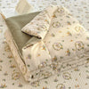 A stack of light beige and olive green cartoon pattern kids lightweight summer quilts on a white quilted surface.