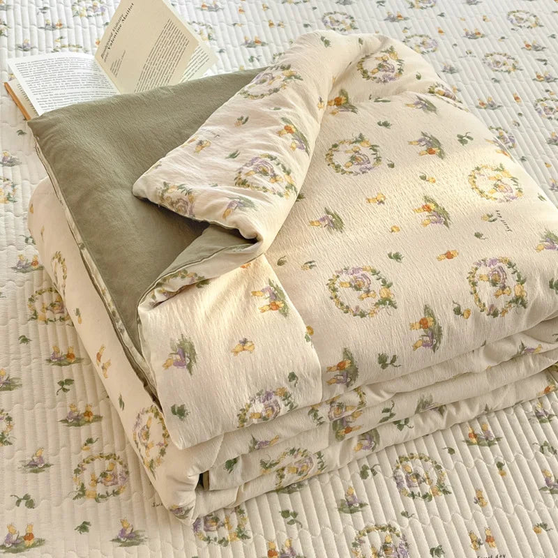 A stack of light beige and olive green cartoon pattern kids lightweight summer quilts on a white quilted surface.
