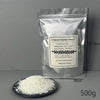 A bag of Natural Soybean Wax flakes next to a pile of white wax on a dark plate.