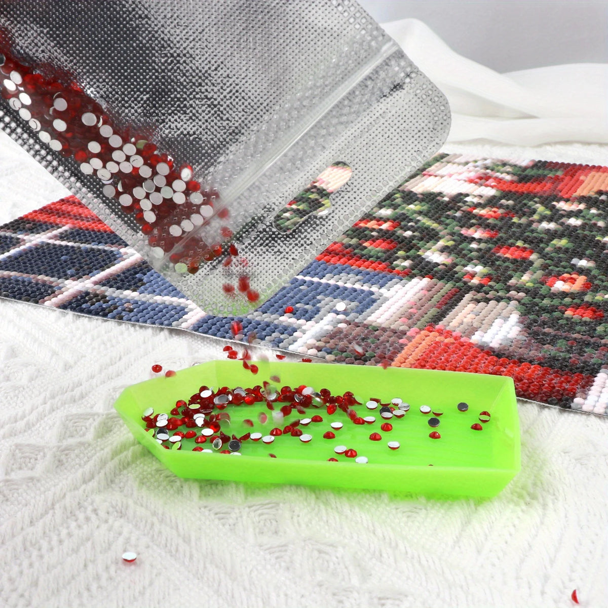 A transparent storage bag is pouring red and silver sequins onto a green plastic tray on a white surface.