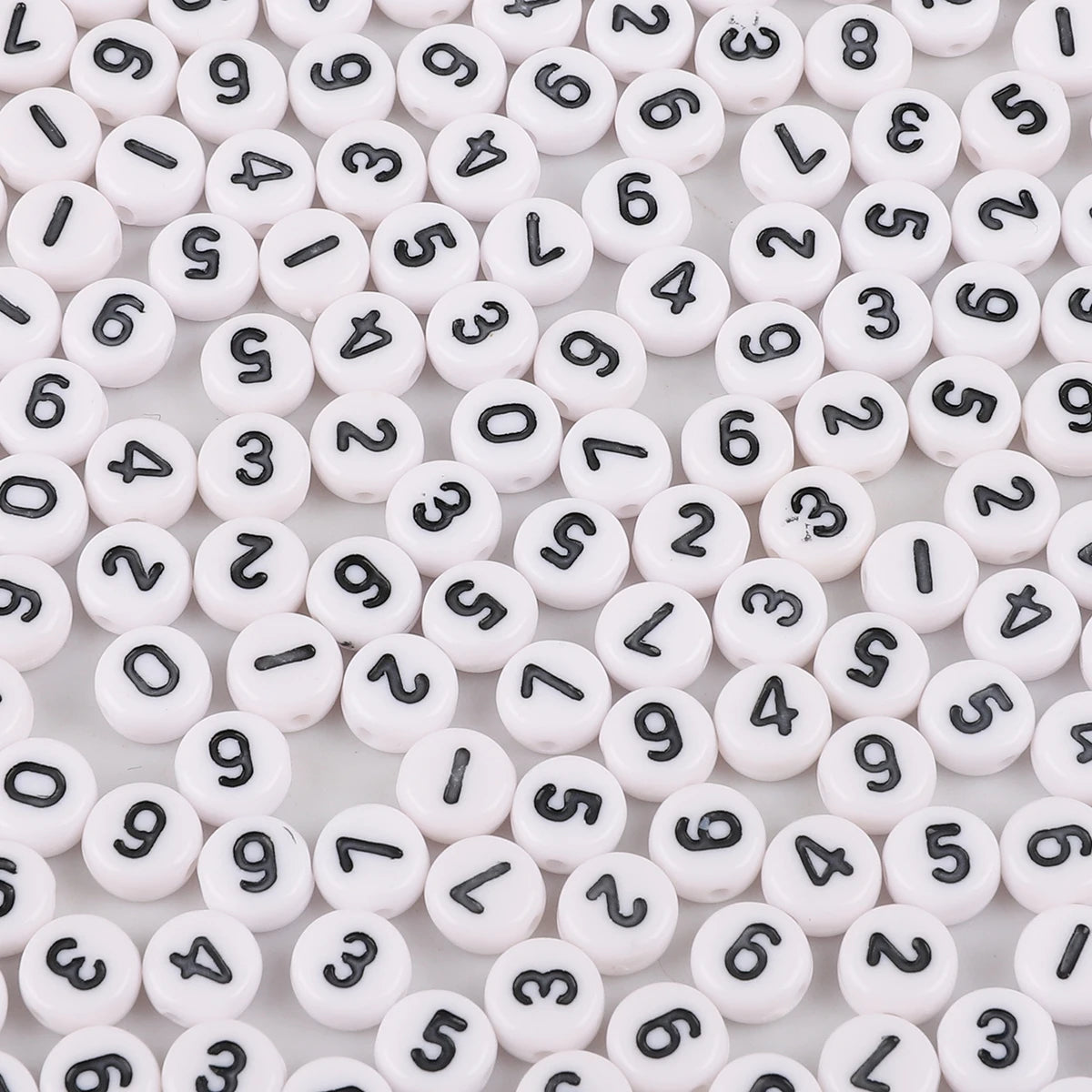 A close-up view of numerous white acrylic alphabet letter beads scattered on a white surface.