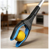 A close-up of a black and blue foldable grabber tool is shown gripping a yellow ball on a light surface.