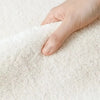 A hand is gently touching a thick, white, fluffy mat rug.