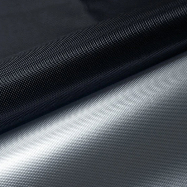 A close-up of a black blackout curtain fabric rolled, showing a transition to a light gray material.