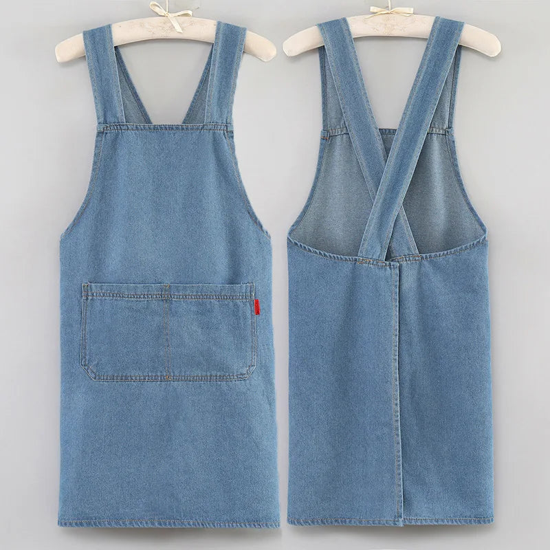 A pair of light blue denim cross-back aprons displayed on hangers.