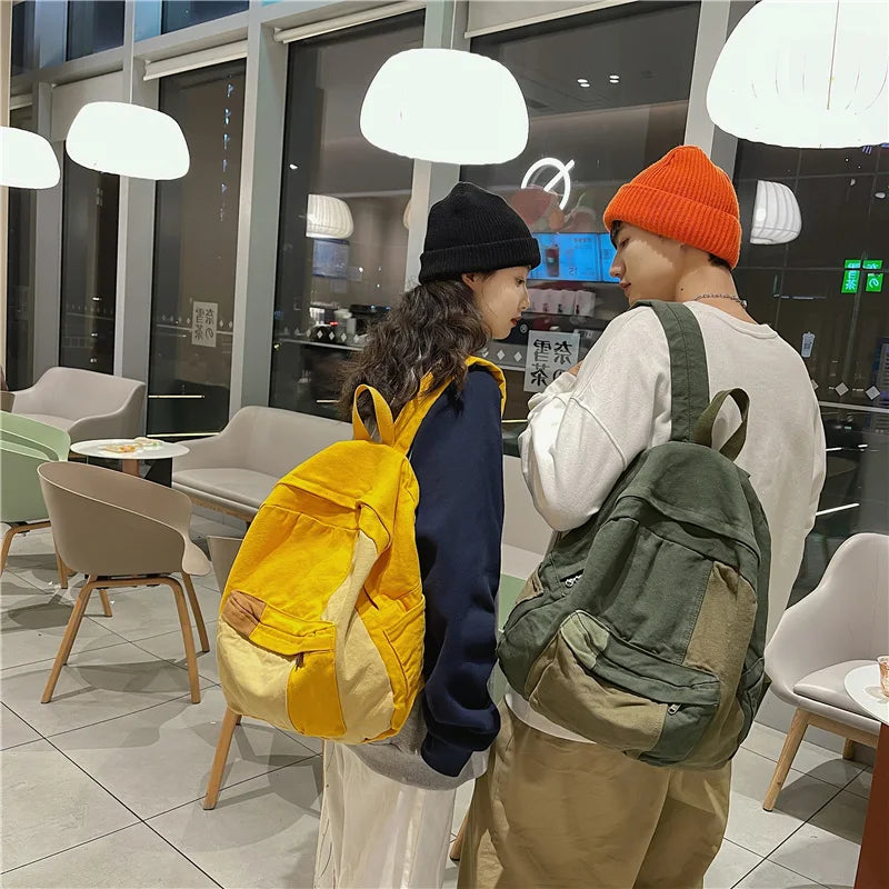 Two people wearing canvas patchwork backpacks stand in a modern indoor space.