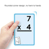 A hand holds a blue math practice card showing the multiplication problem 7 x 4 and another card showing 13 x 5/65.