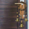 A rustic witch bells door hanger wind chime with brass bells and wooden accents hanging on a dark brown door.