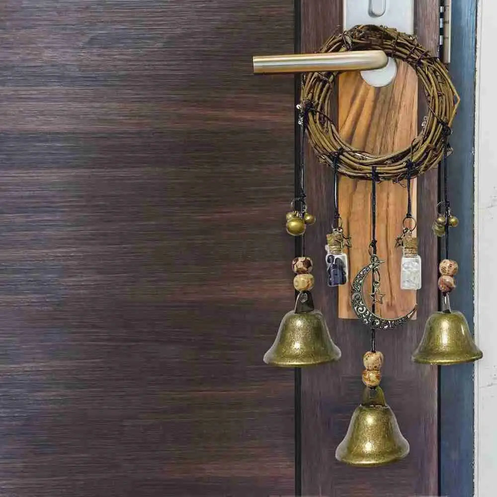 A rustic witch bells door hanger wind chime with brass bells and wooden accents hanging on a dark brown door.