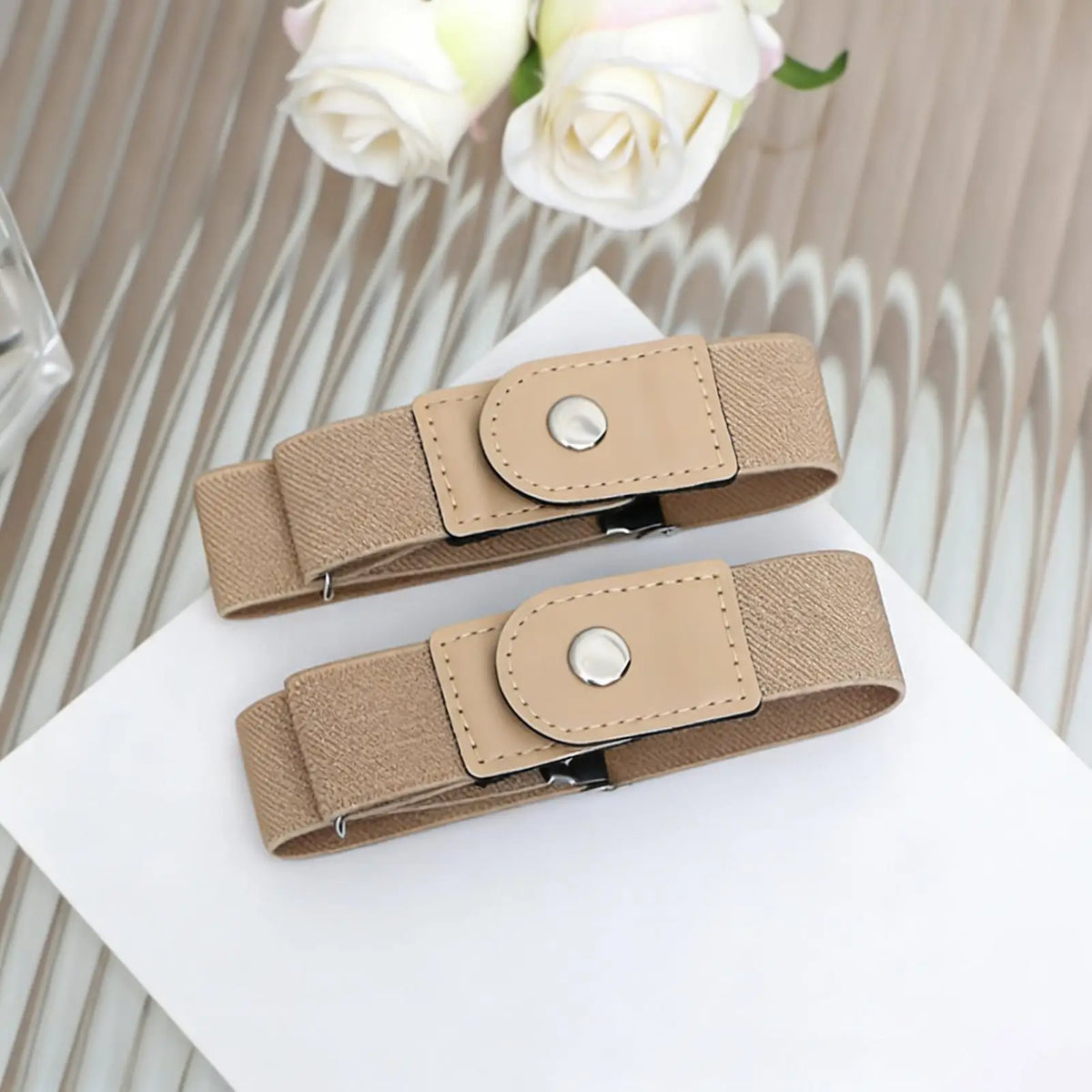 A pair of beige elastic belts with leather accents are displayed on a white surface.