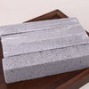 A rectangular block of gray pumice stone cleaning stick resting on a dark wooden surface.