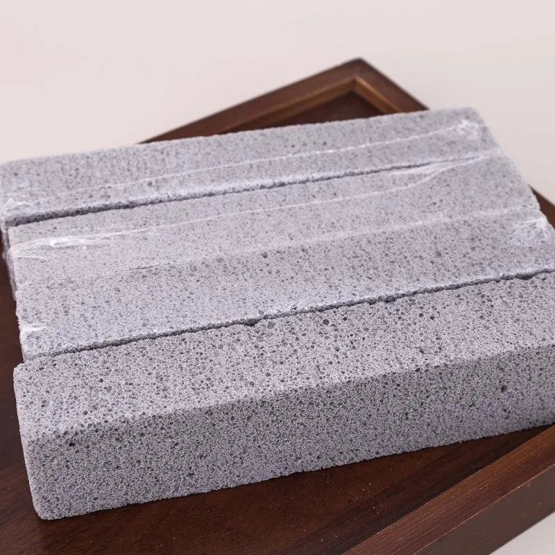 A rectangular block of gray pumice stone cleaning stick resting on a dark wooden surface.