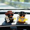 A rubber duck car ornament featuring a cowboy hat and sunglasses sits on a dashboard.