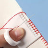 A hand is using a white sewing guide template with red thread and a needle to mark stitches on fabric.
