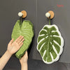 A green leaf-shaped coral fleece hand towel with a hanging loop is displayed against a dark gray background.