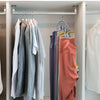 A row of clothing hangers in a closet displaying various colored shirts and sweaters.