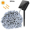 A black solar-powered outdoor string light with numerous LED bulbs is shown next to a solar panel.