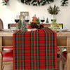A red tartan Christmas table runner with green and black plaid pattern on a wooden table.