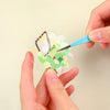 Hands use blue tweezers to place macaron color craft elements onto a sheet for scrapbooking