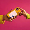 A hand holds a yellow silicone suction cup phone holder mat against a pink background.