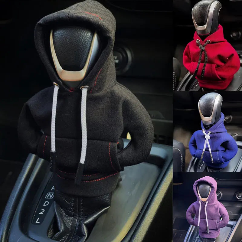 Una sudadera negra con capucha y cordón está colocada en un pomo de palanca de cambios del coche.