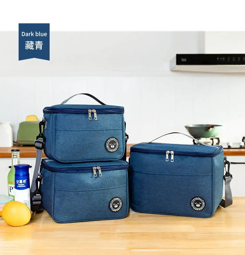 Two dark blue insulated lunch bags with shoulder straps resting on a wooden surface.