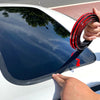 A hand is installing a black rubber seal strip on the edge of a car window.