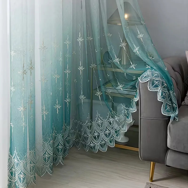 A sheer teal curtain with floral embroidery hangs next to a gray sofa.