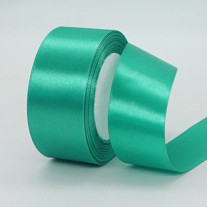 A roll of teal green satin ribbon used for gift wrapping or DIY crafts.