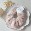 A pair of soft, light pink plush coil hair ties made of stainless steel resting on a white plate.