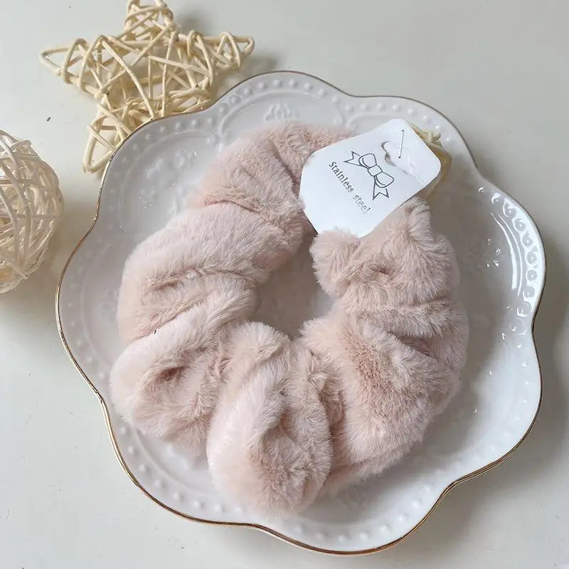 A pair of soft, light pink plush coil hair ties made of stainless steel resting on a white plate.