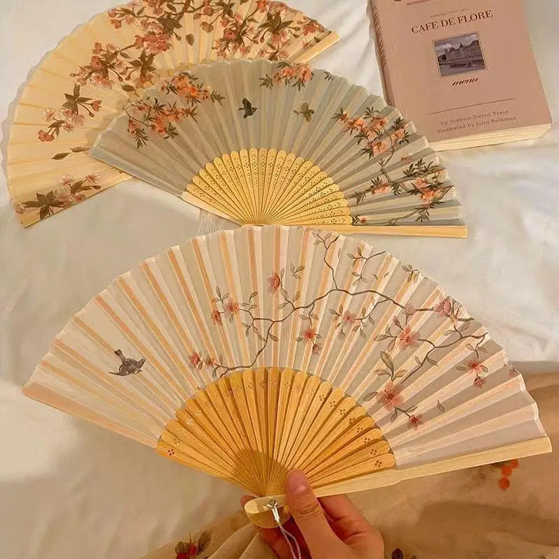 A light wood folding fan with a floral design is displayed on a white cloth.