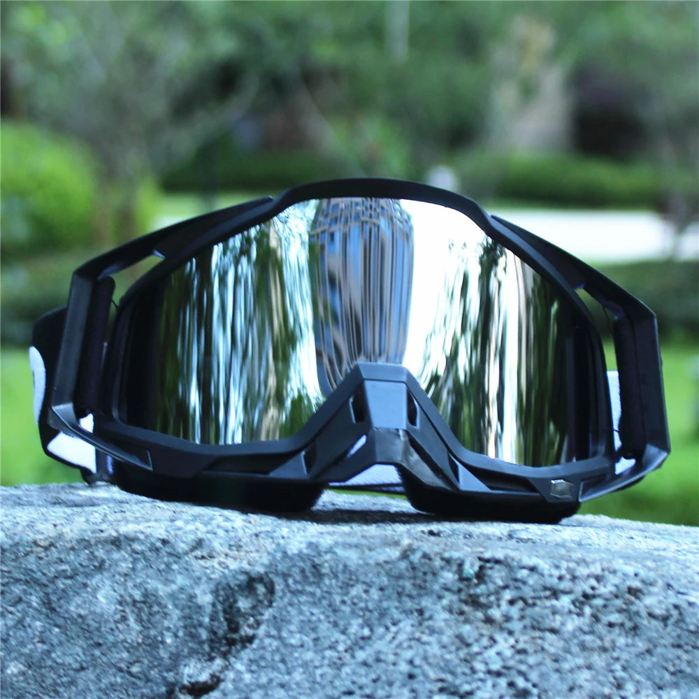 A pair of black retro motorcycle sunglasses with night vision lenses resting on a gray stone.