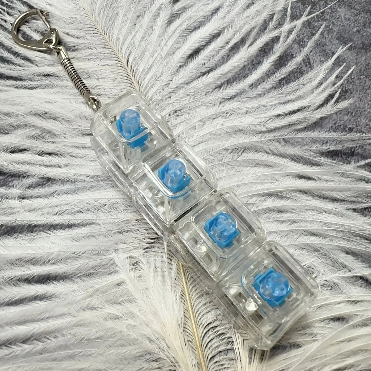 Clear plastic keychain with blue LED lights and a metal loop, resting on white feathers.