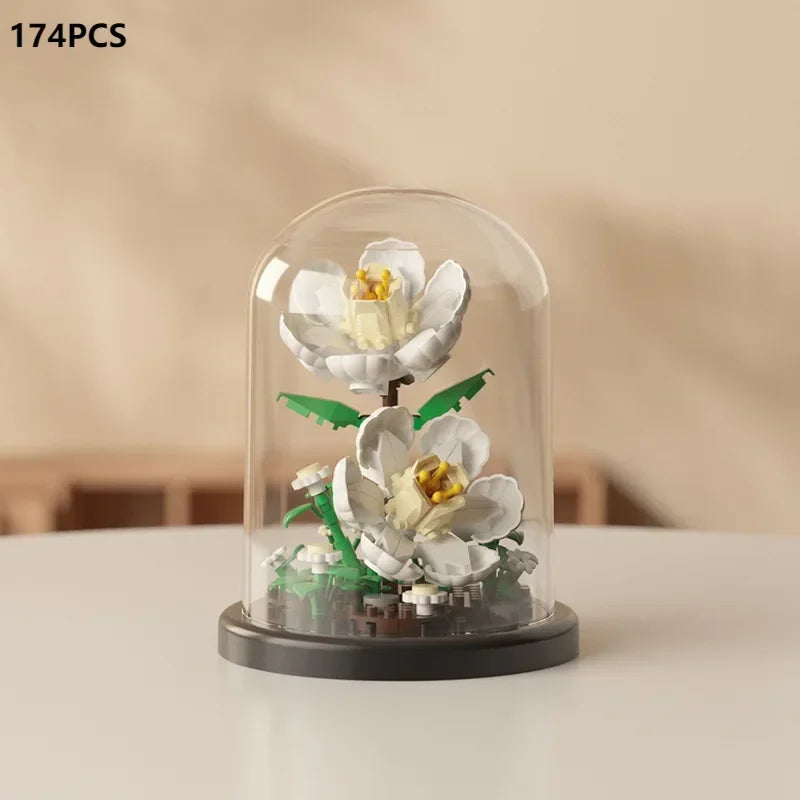 A clear glass display featuring a miniature white rose bouquet built from building blocks.