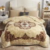 A beige weighted plush raschel blanket with brown decorative embroidery is displayed on a bed.